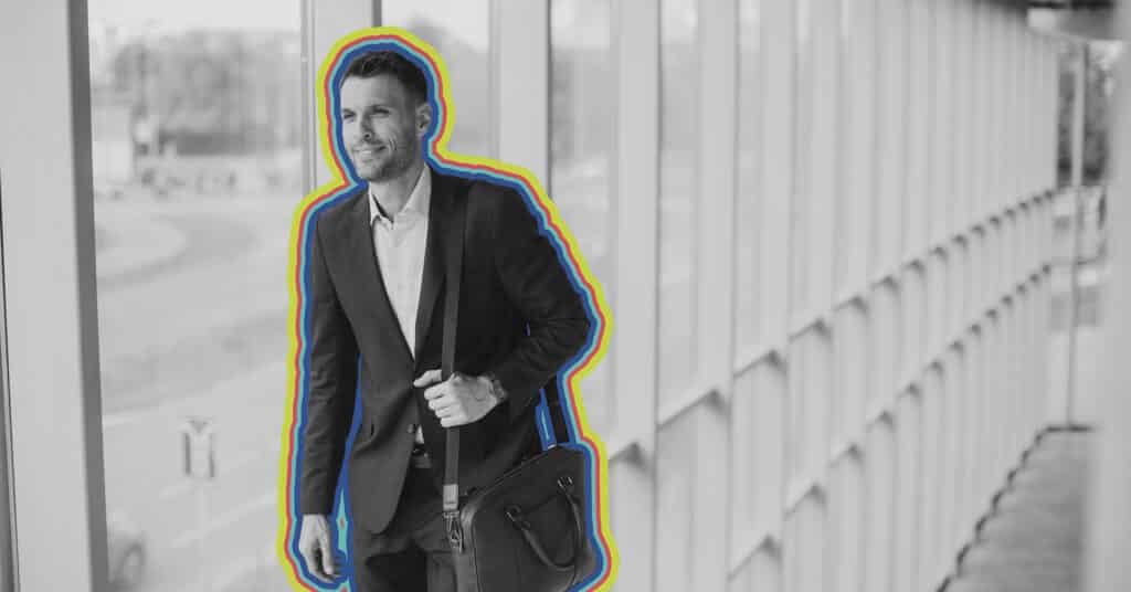 A businessman walks down a well lit corridor with a briefcase, in black and white accented by rainbow lines, illustrating the idea of audience segmentation