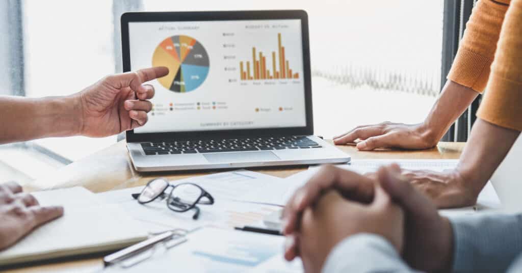 closeup of busy hands of diverse team members discussing data on a laptop and in paper files on a conference table
